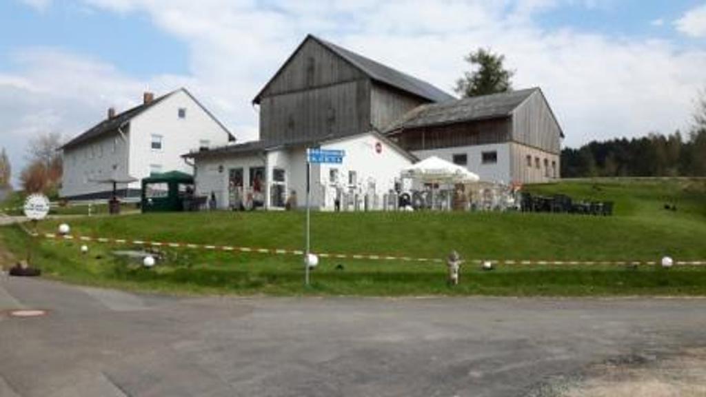 Ein großes weißes Haus steht auf einem grasbewachsenen Hügel neben einer Straße.