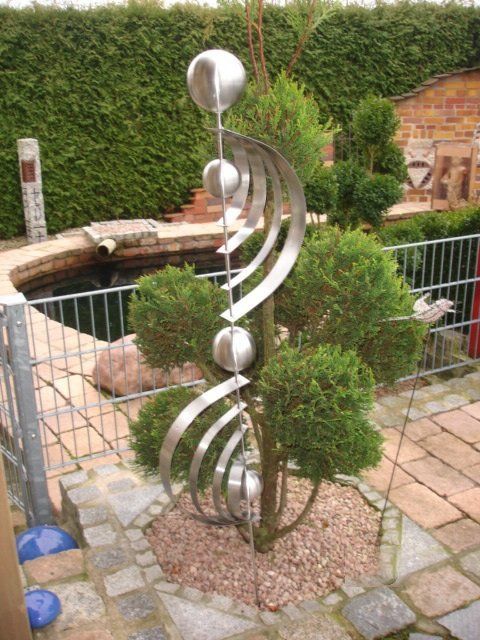 Eine Edelstahlskulptur sitzt neben einem Baum