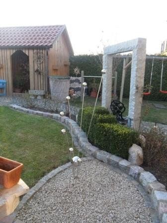 Ein Hinterhof mit Holzschuppen, Schaukeln und einem Kiesweg.