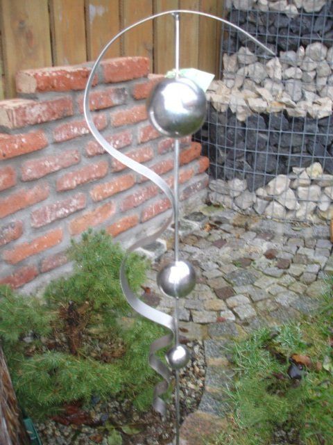 Eine Metallskulptur in einem Garten mit einer Backsteinmauer im Hintergrund