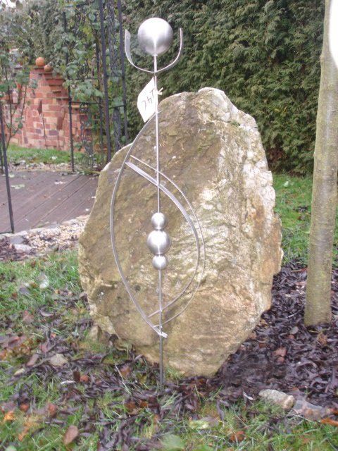 Auf einem großen Felsen im Gras sitzt eine Skulptur.