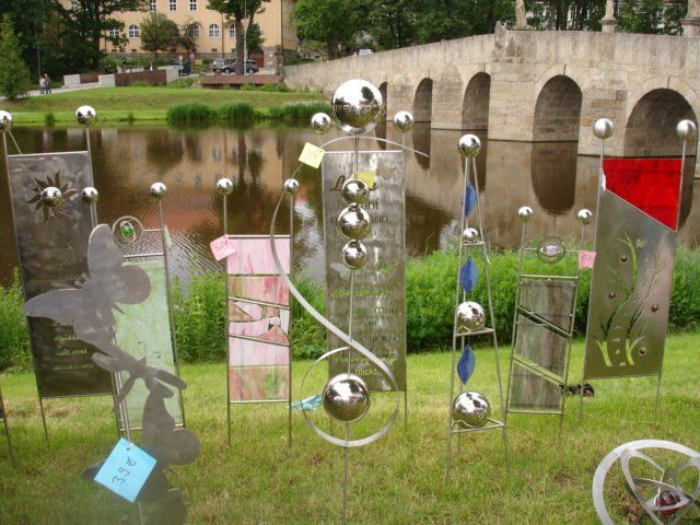 Ein Haufen Metallskulpturen sitzt im Gras in der Nähe eines Gewässers