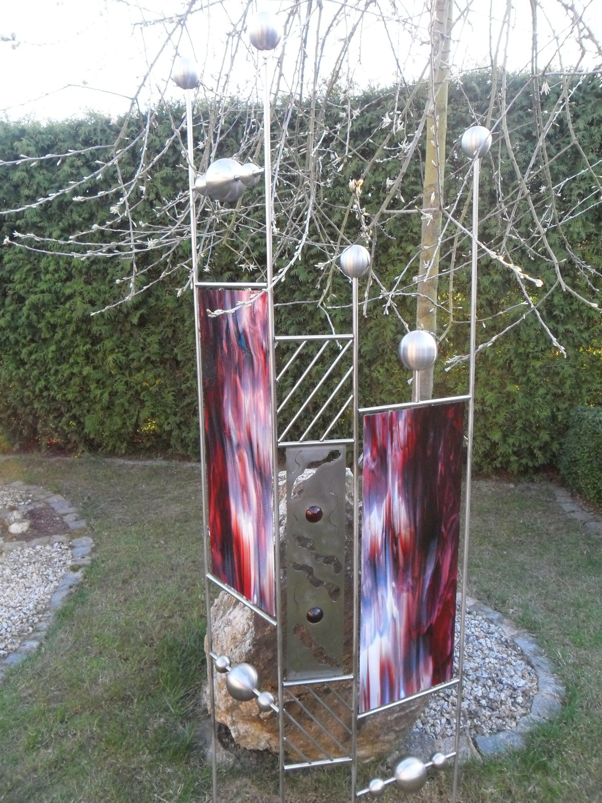 Eine Edelstahlskulptur mit einem Baum im Hintergrund