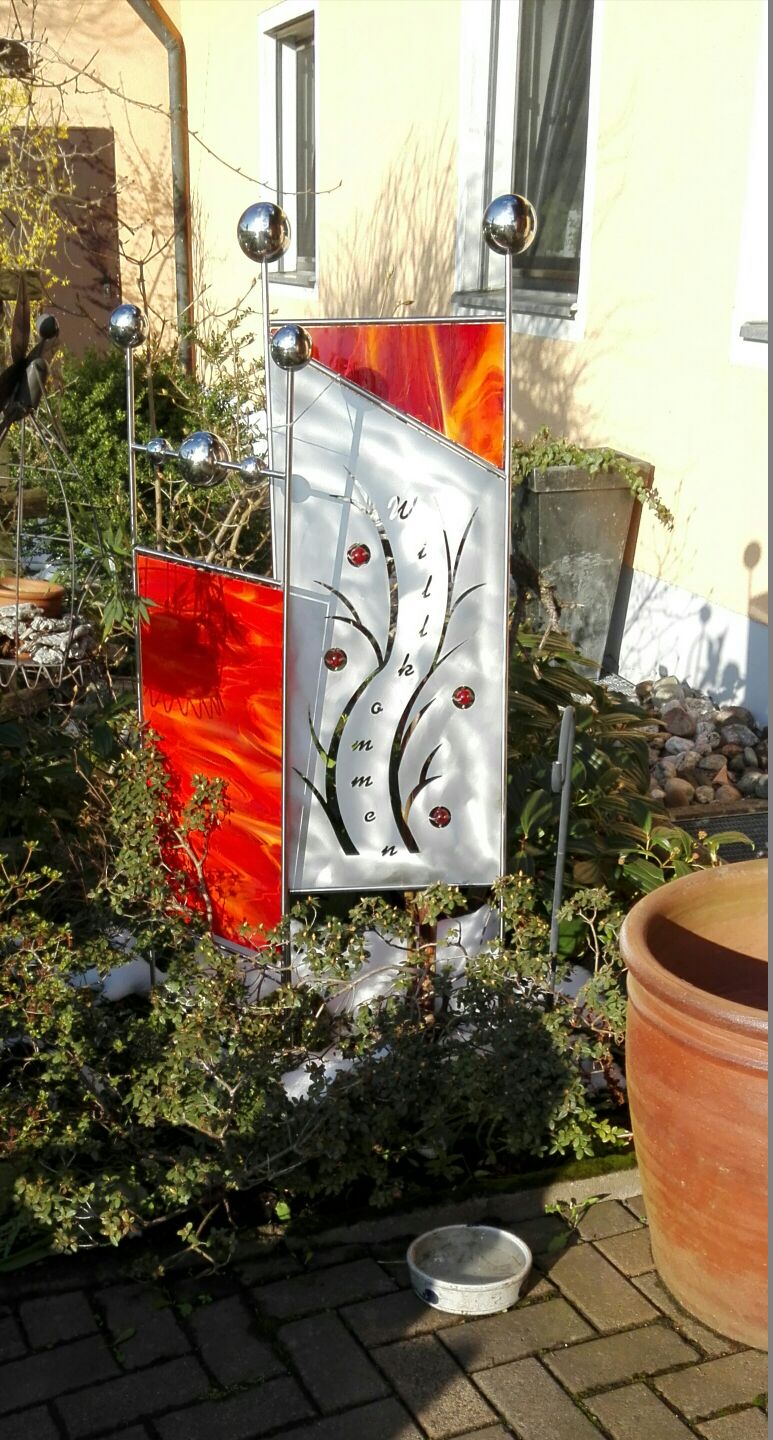 Eine rot-weiße Skulptur steht auf einem Backsteingehweg vor einem Haus.