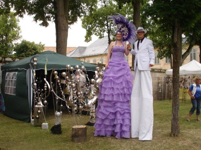 Eine Frau in einem lila Kleid steht neben einem Mann auf Stelzen