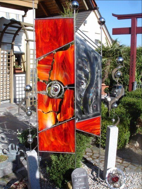 Eine Buntglas-Skulptur in einem Garten mit einem roten Torii-Tor im Hintergrund