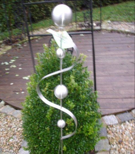 Auf der Spitze eines kleinen Busches sitzt eine Skulptur aus Edelstahl.