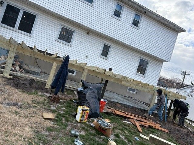 A group of people are working on a wooden deck in front of a house.
