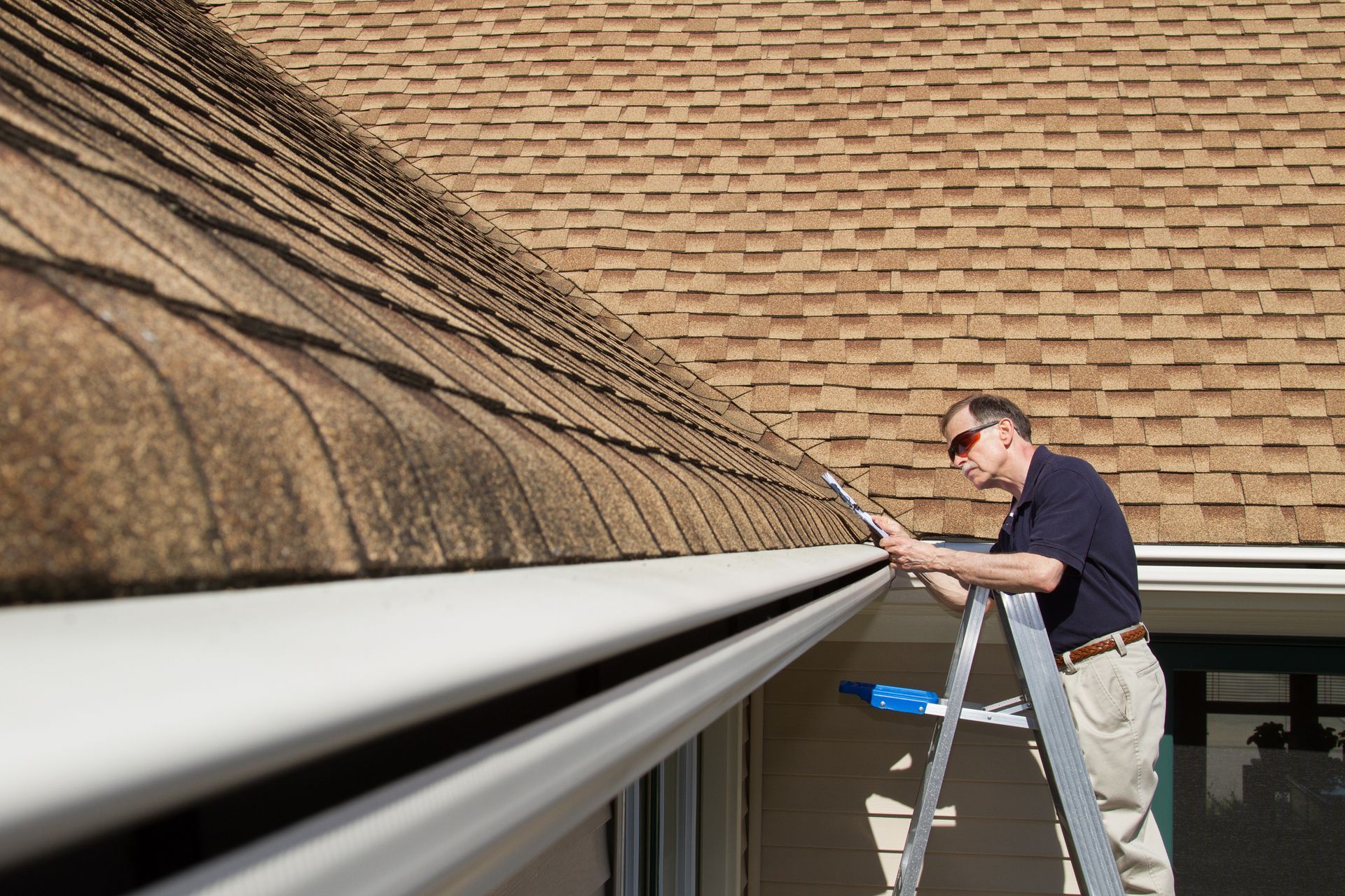 A man on a ladder is cleaning a gutter on a roof.