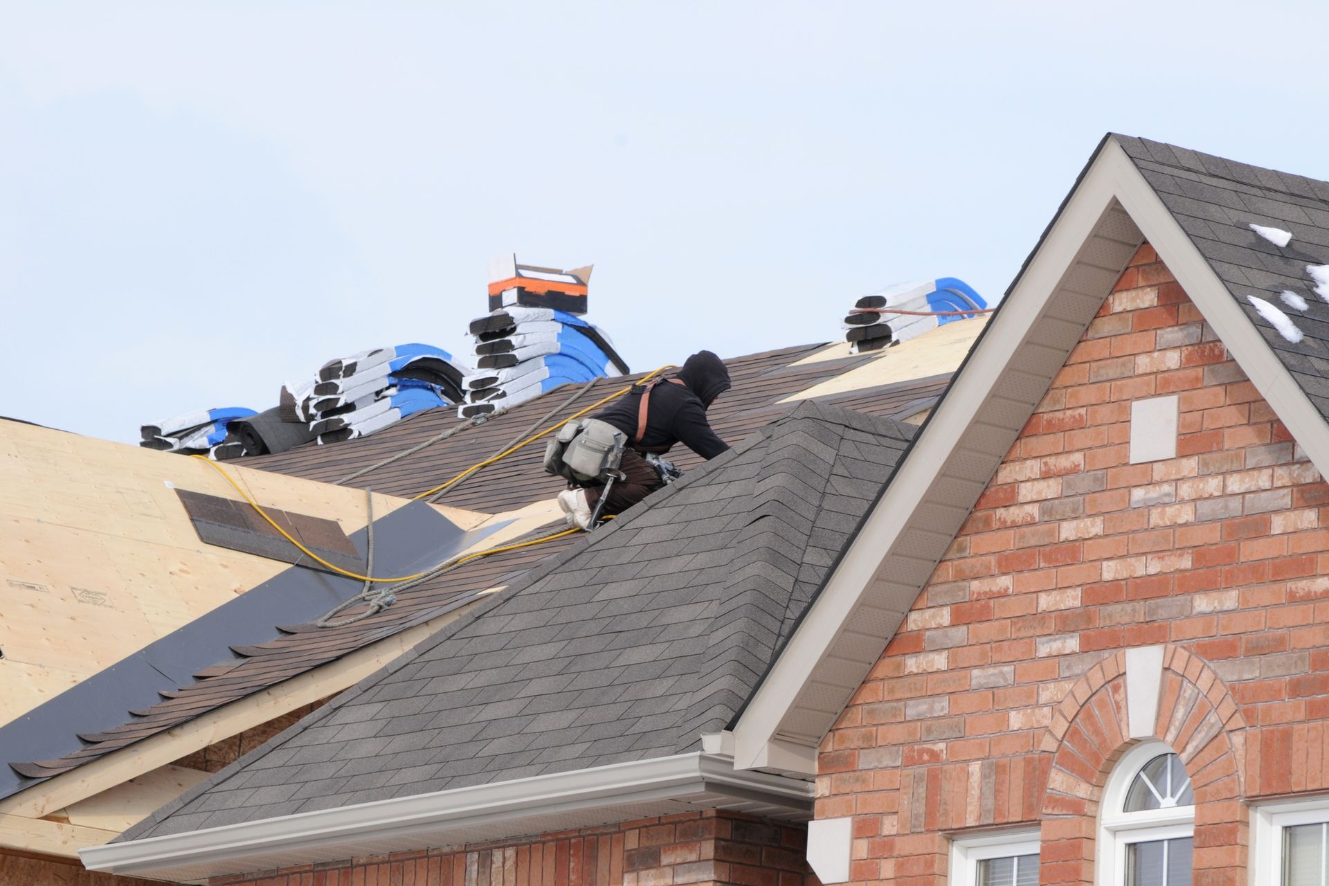 A man is working on the roof of a brick house.
