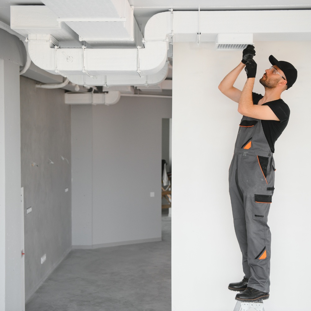 Man cleaning air duct with a vacuum hose.