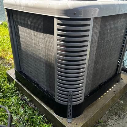 Air conditioner unit outside, black, gray and green, on concrete base.