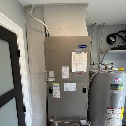 An HVAC unit next to a water heater in a utility room. Gray metal machines.