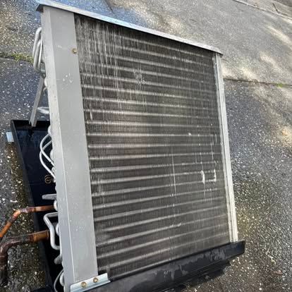 Air conditioning condenser coil with copper tubes and metal frame on a gray surface.