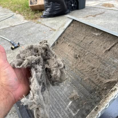 Hand holding a large clump of dust removed from a dirty HVAC filter.