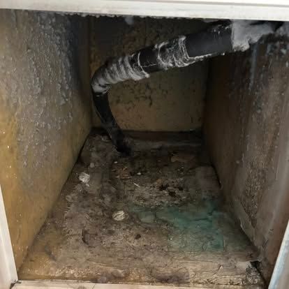 Inside of dirty ductwork with a black pipe. The floor is stained, and the walls are dusty.