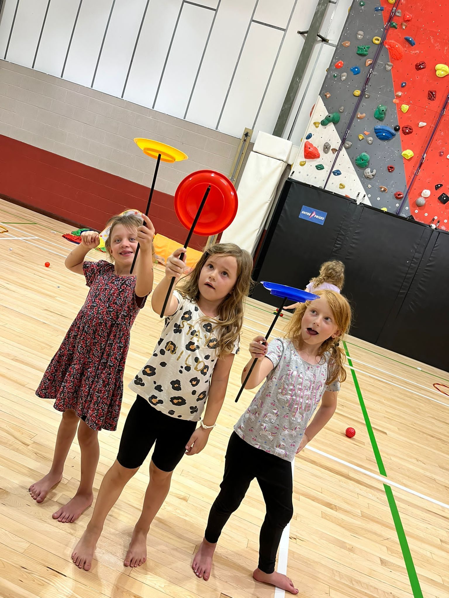 Three young girls are holding plates in a gym.