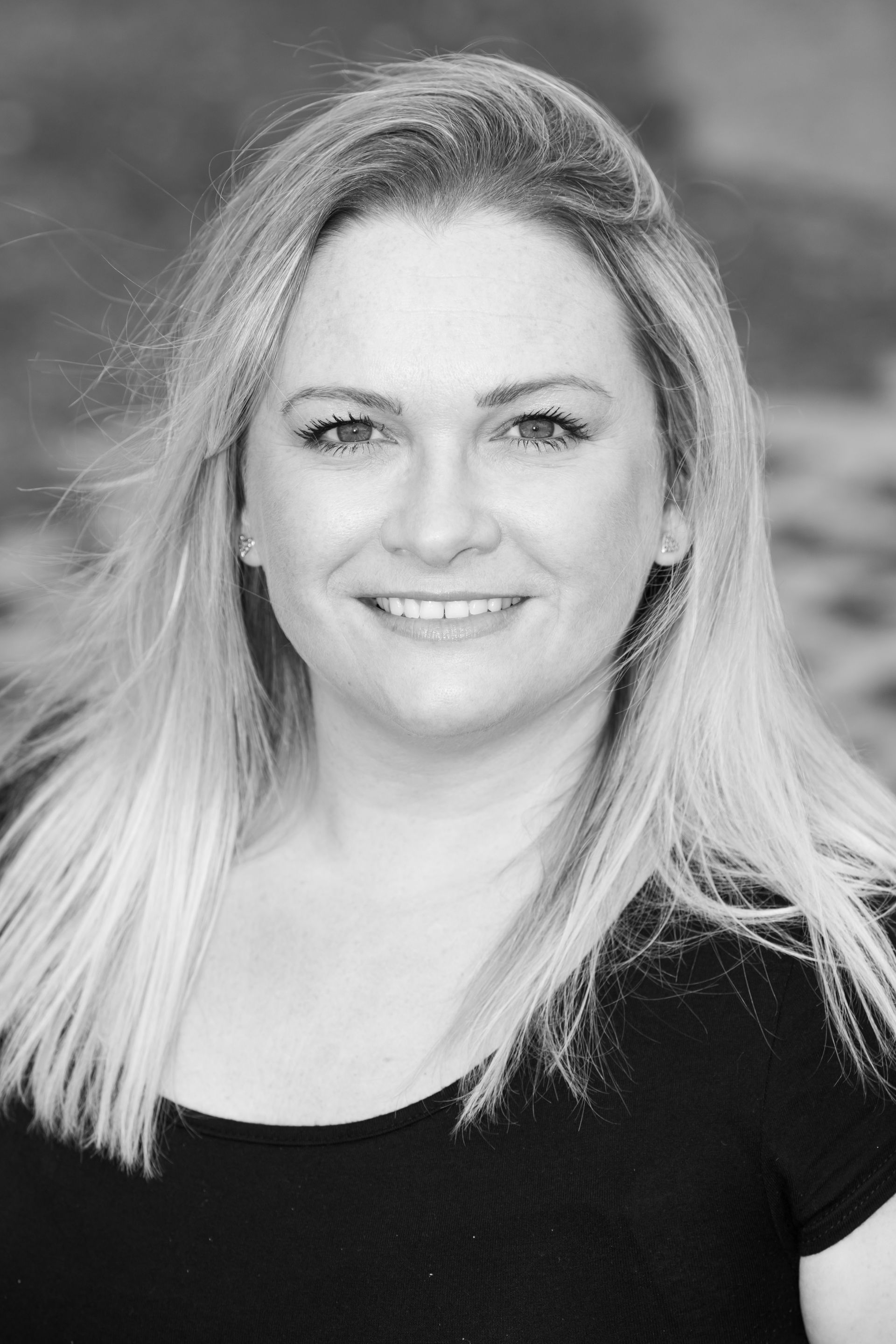 A woman with long blonde hair is smiling in a black and white photo.