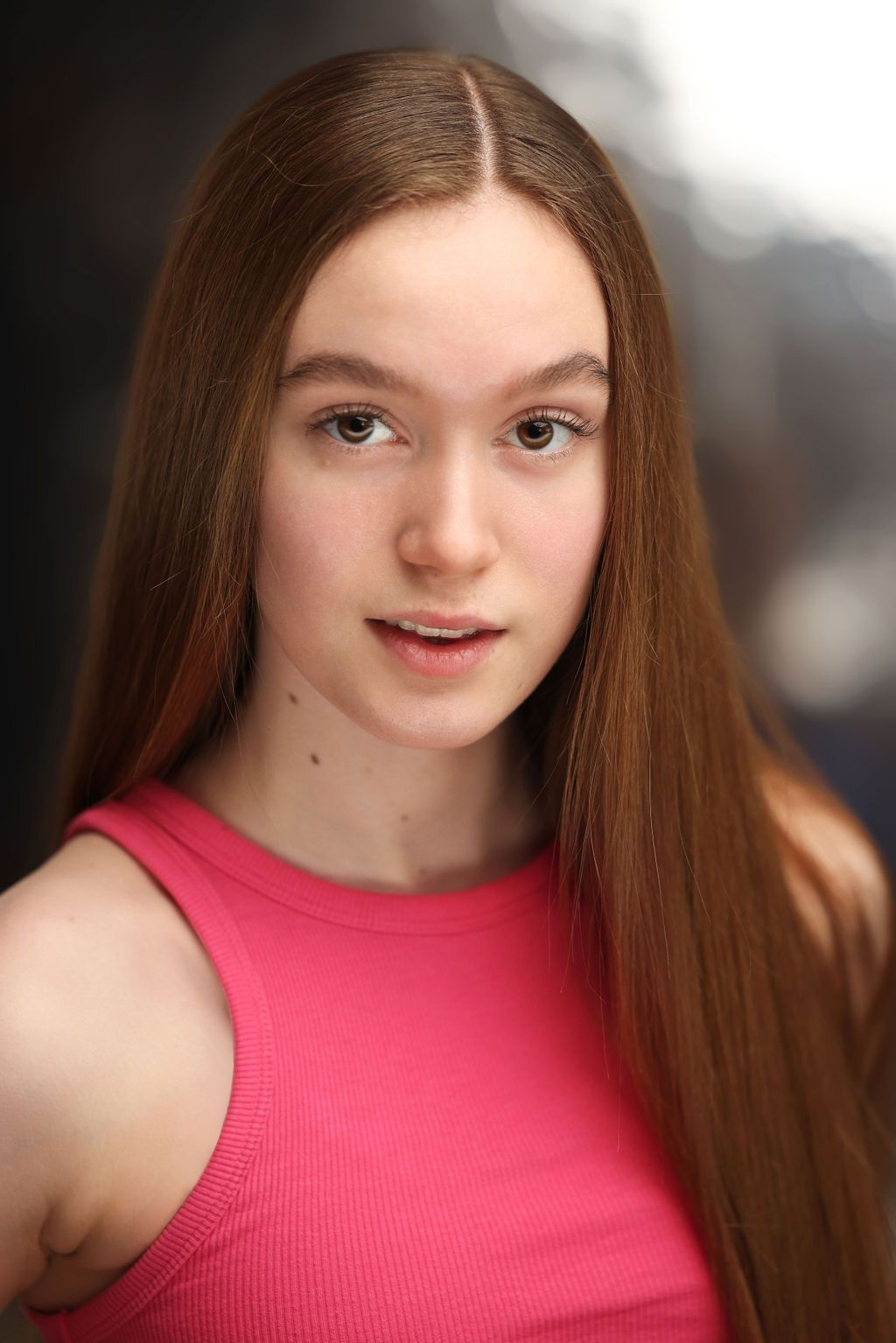 A young girl with long brown hair is wearing a pink tank top.