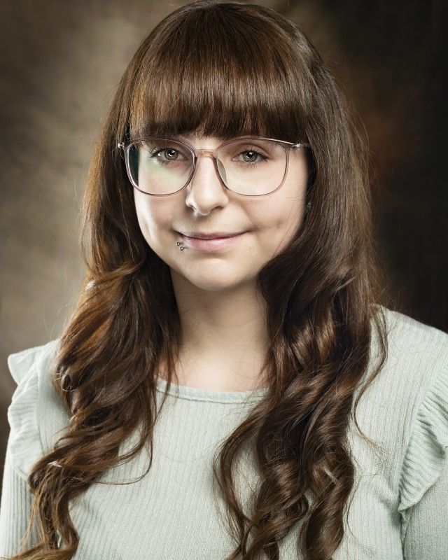 A woman with long hair and glasses is smiling for the camera.