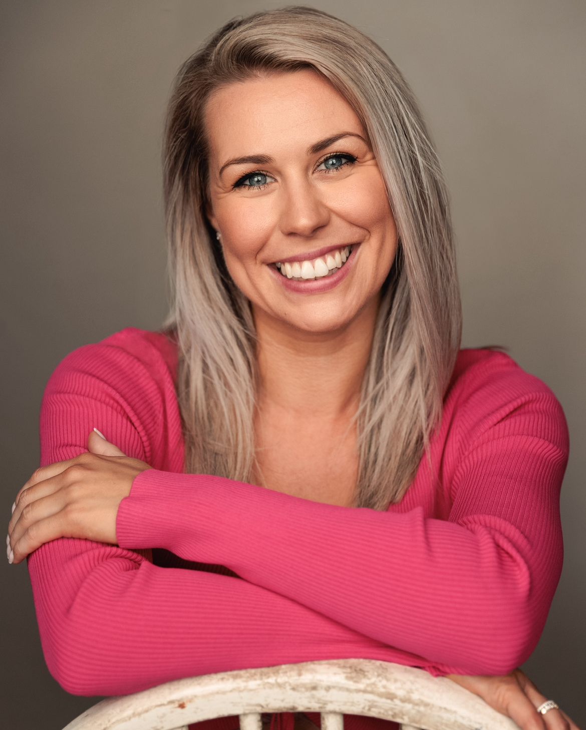 A woman in a pink sweater is sitting in a chair with her arms crossed and smiling.
