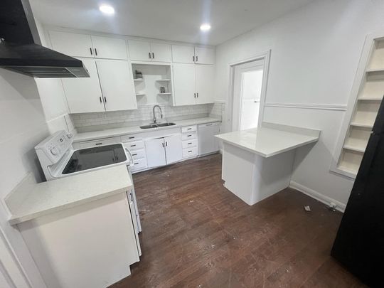 Bright white kitchen with dark wood floor, island, sink, stove, and open shelving