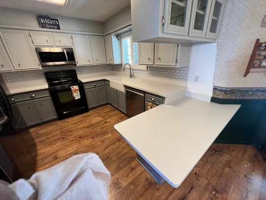 Modern white kitchen with black stove, wood floors, and a breakfast bar area