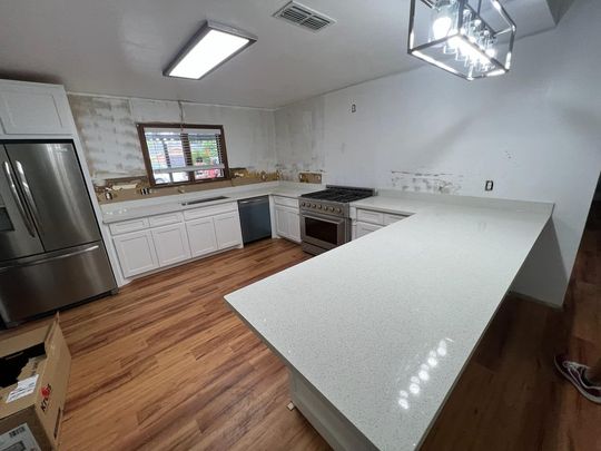 Modern kitchen with white counters, wood floors, stainless fridge, and a large island under pendant lights