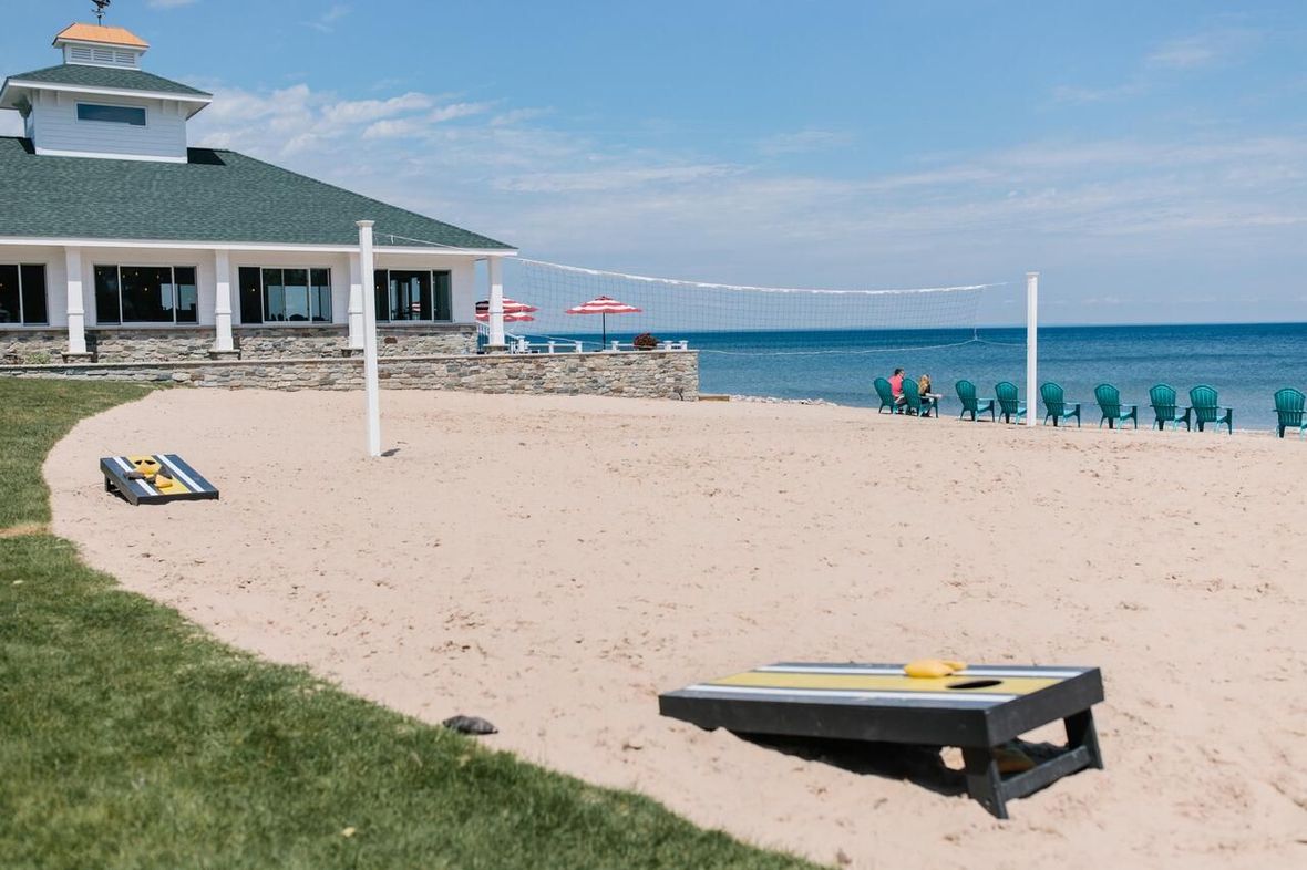 A sandy beach with a volleyball net and a cornhole board.