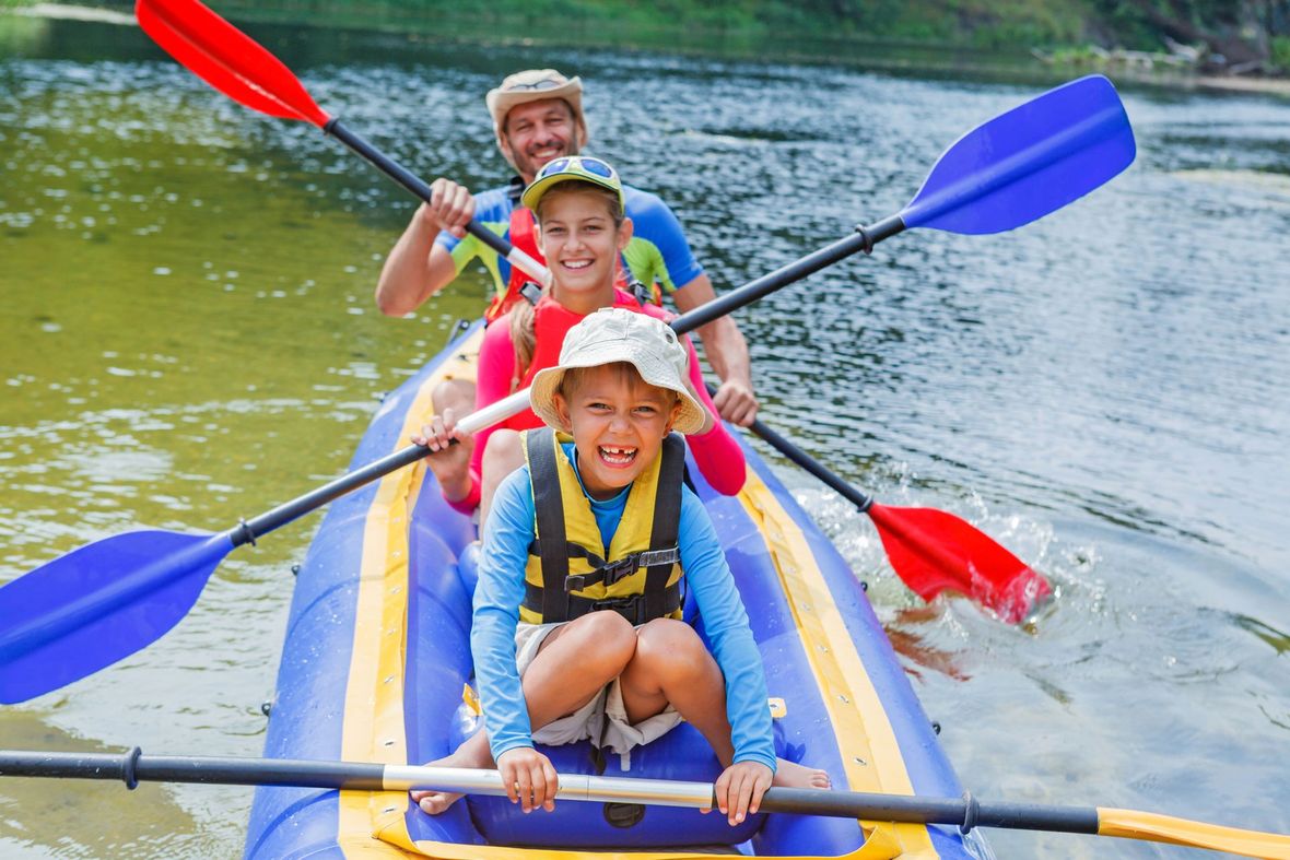 A man and two children are paddling a kayak on a river.