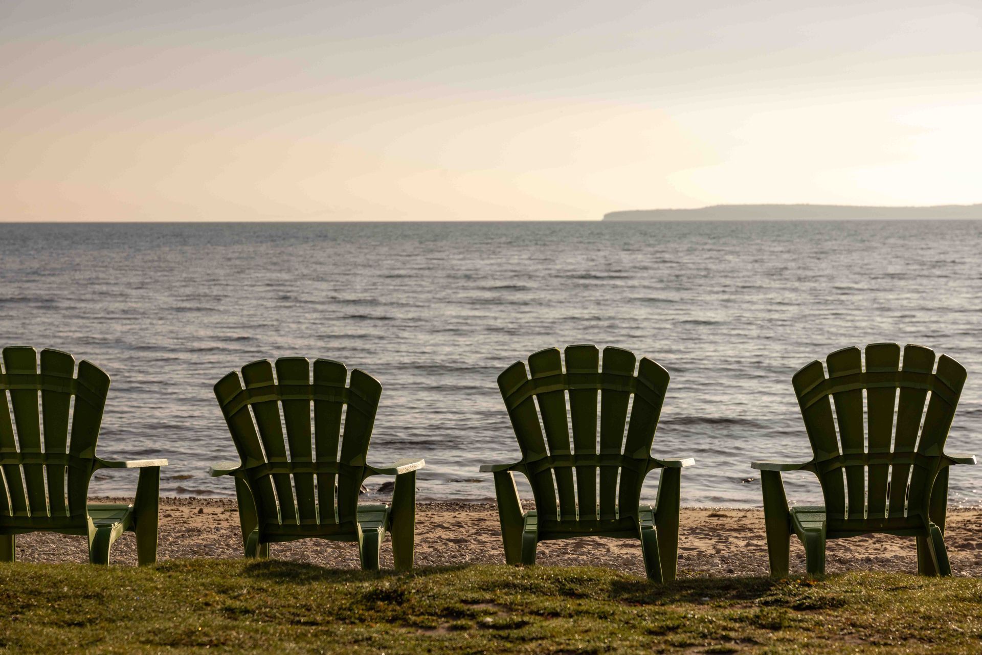 A row of adirondack chairs on a beach with the ocean in the background.