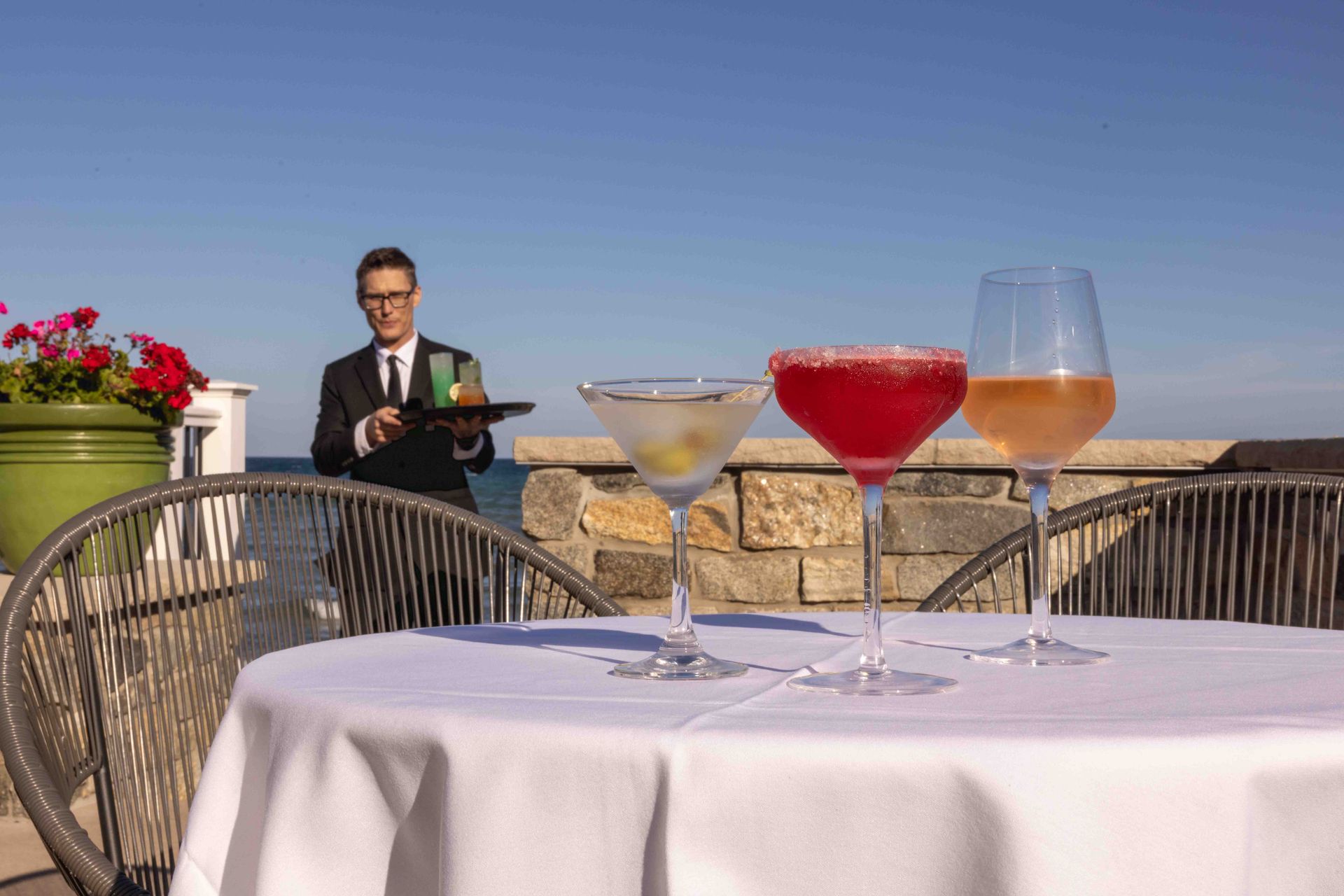 A man is standing behind a table with three drinks on it.
