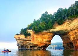 A couple of people in a kayak in front of a large rock formation in the water.