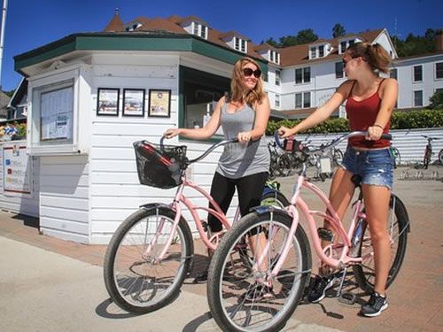 Two women are riding bicycles in front of a building.