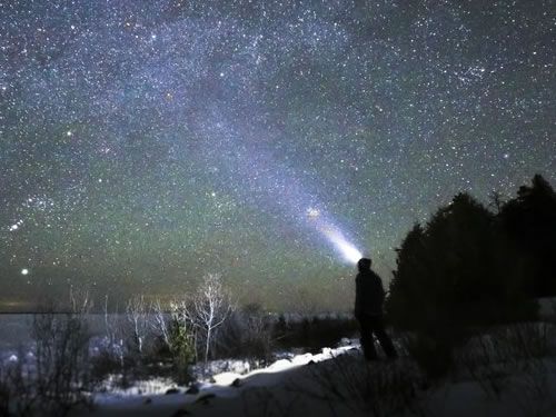 A person is holding a flashlight in front of a starry sky.
