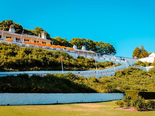 A large white building is sitting on top of a hill surrounded by trees.