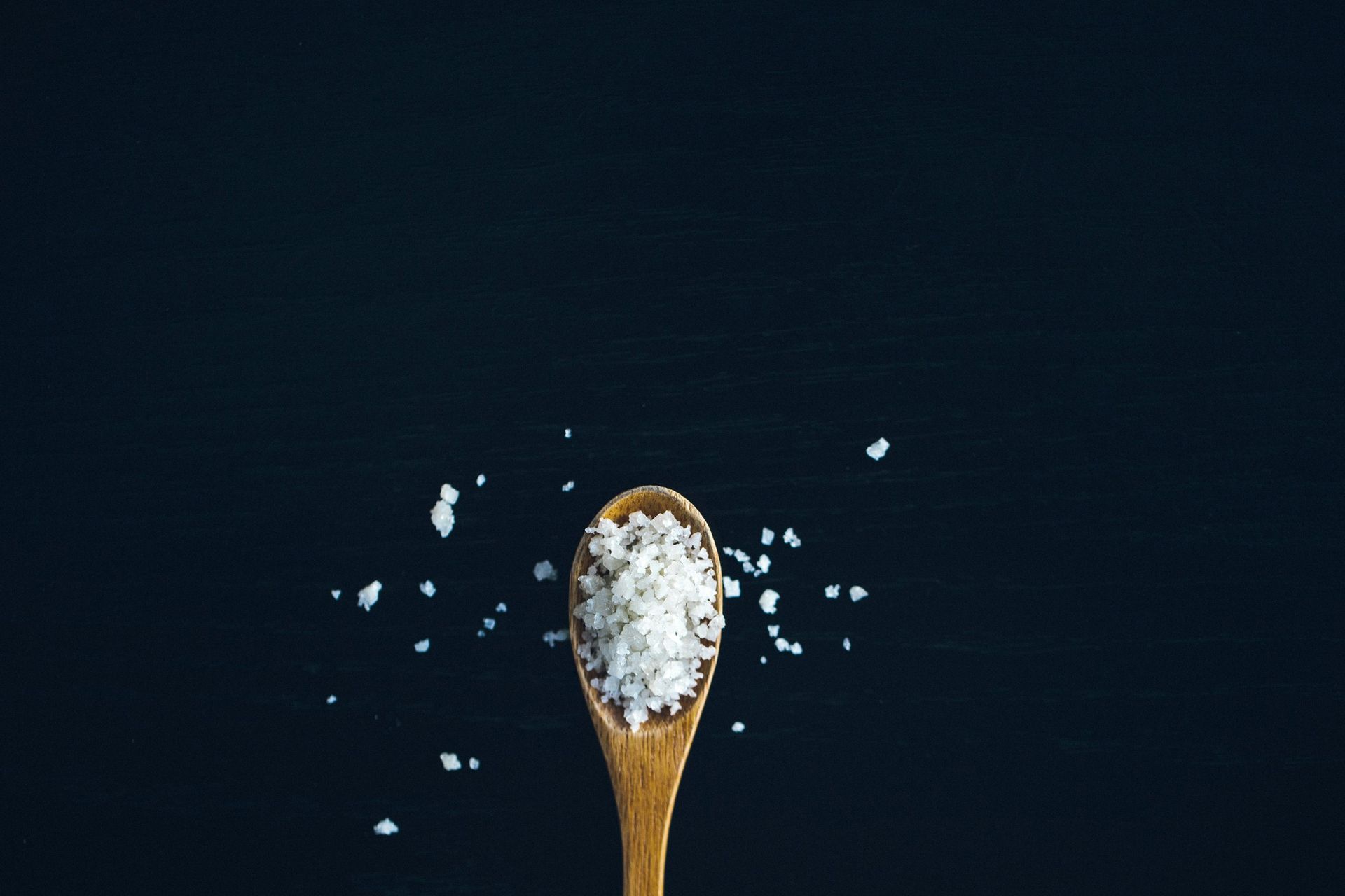 A wooden spoon filled with salt on a black background.