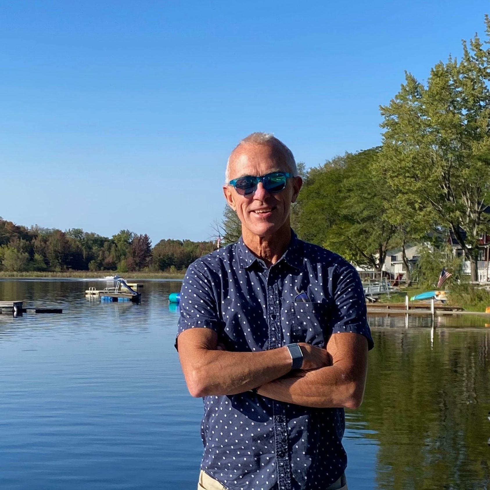 A man is sitting on a stool with his hands folded and smiling.