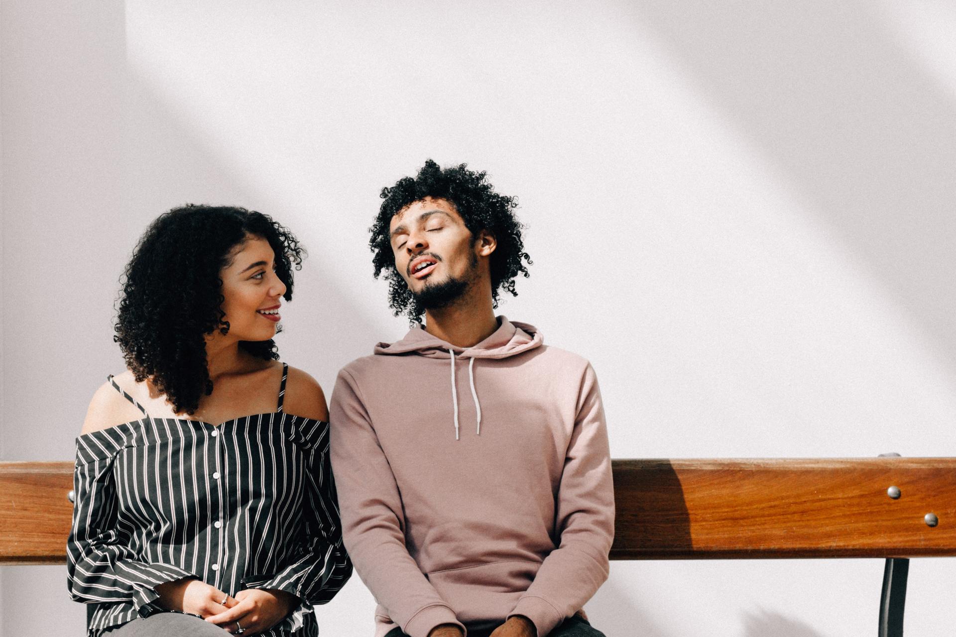 A man and a woman are sitting on a bench talking to each other.