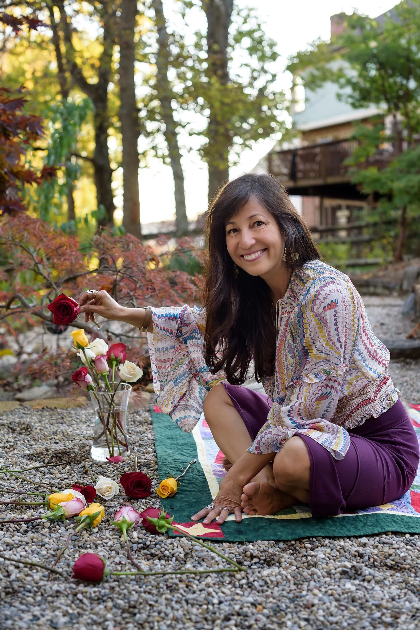 A woman is sitting on a blanket in the dirt surrounded by flowers.