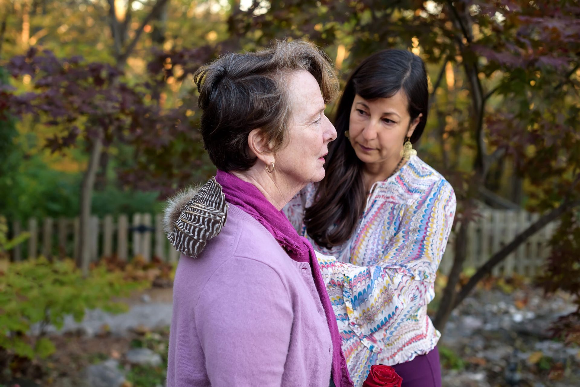 Two women are standing next to each other in a park and talking to each other.