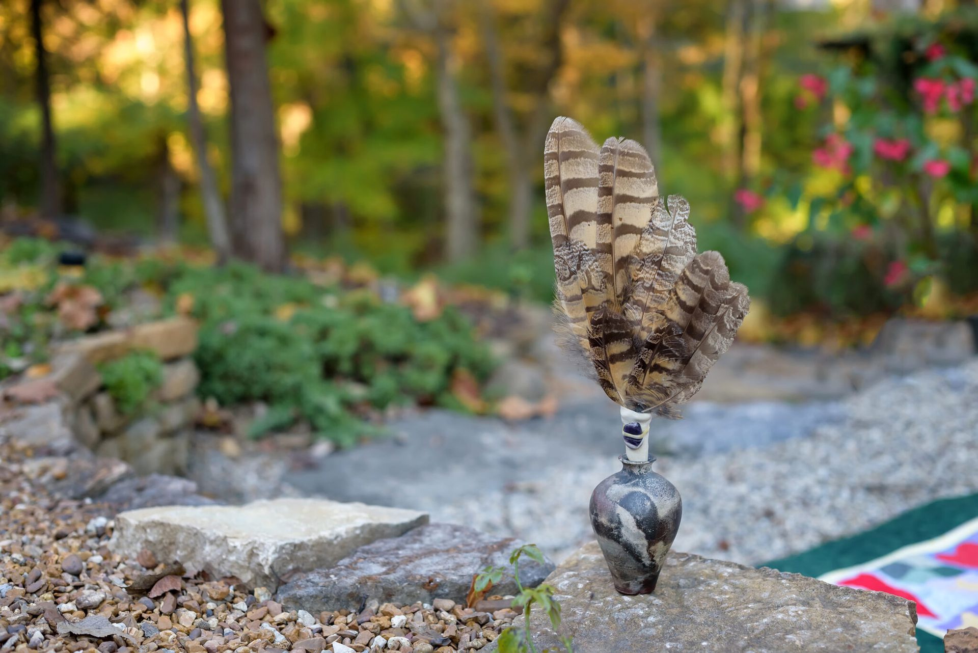 A feather is sitting on top of a small vase on a rock.