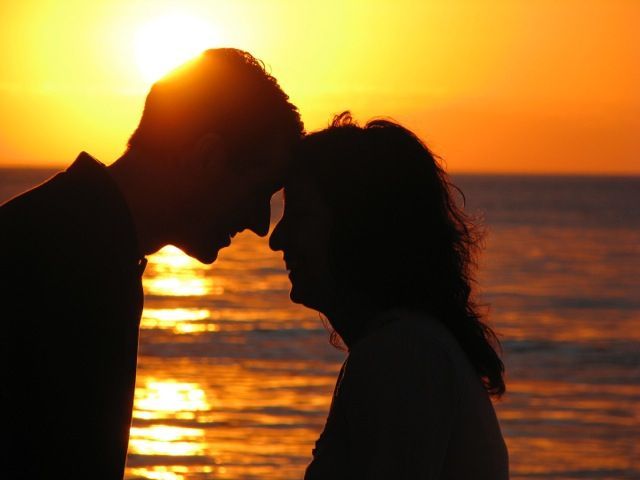 A man and a woman are kissing on the beach at sunset.