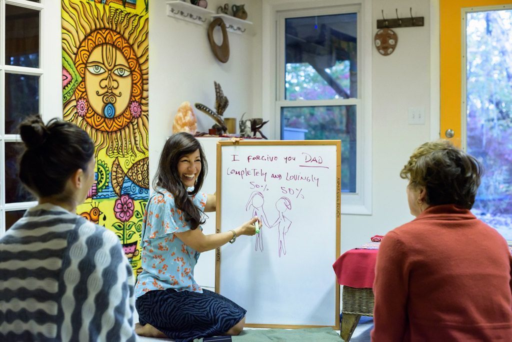 A woman is kneeling down in front of a whiteboard talking to two women.