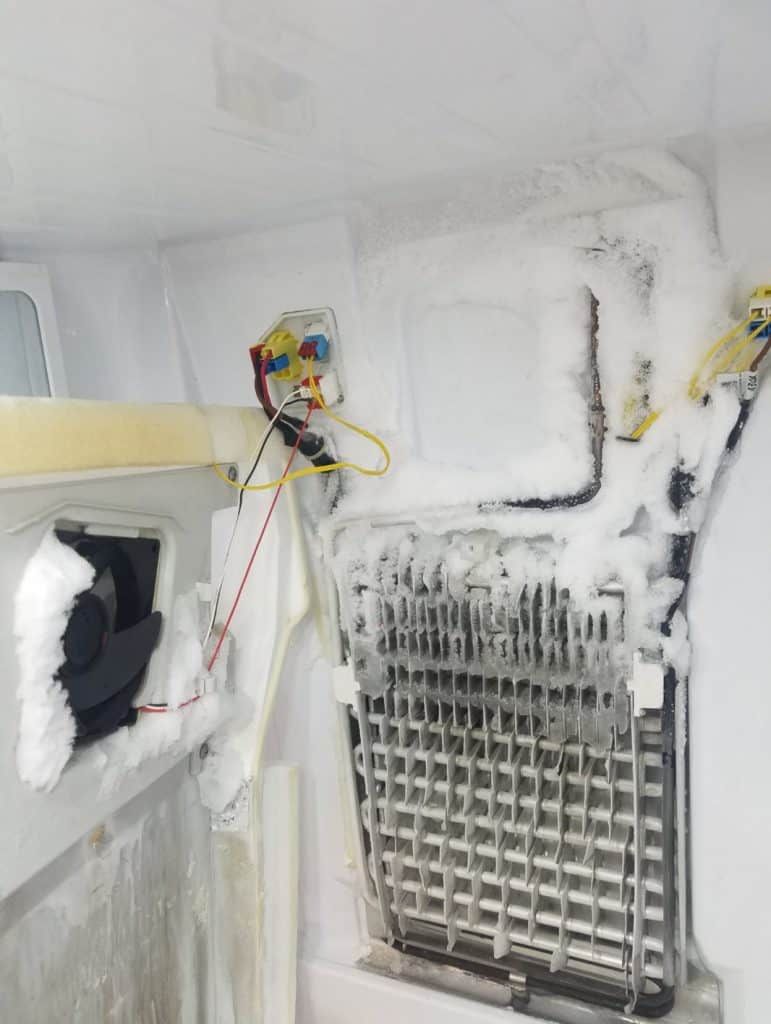 The inside of a refrigerator is covered in ice and snow.