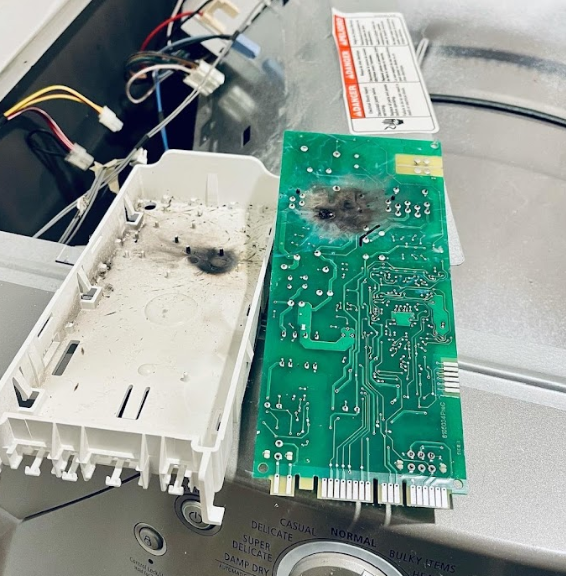 A dirty electronic board is sitting on top of a washing machine