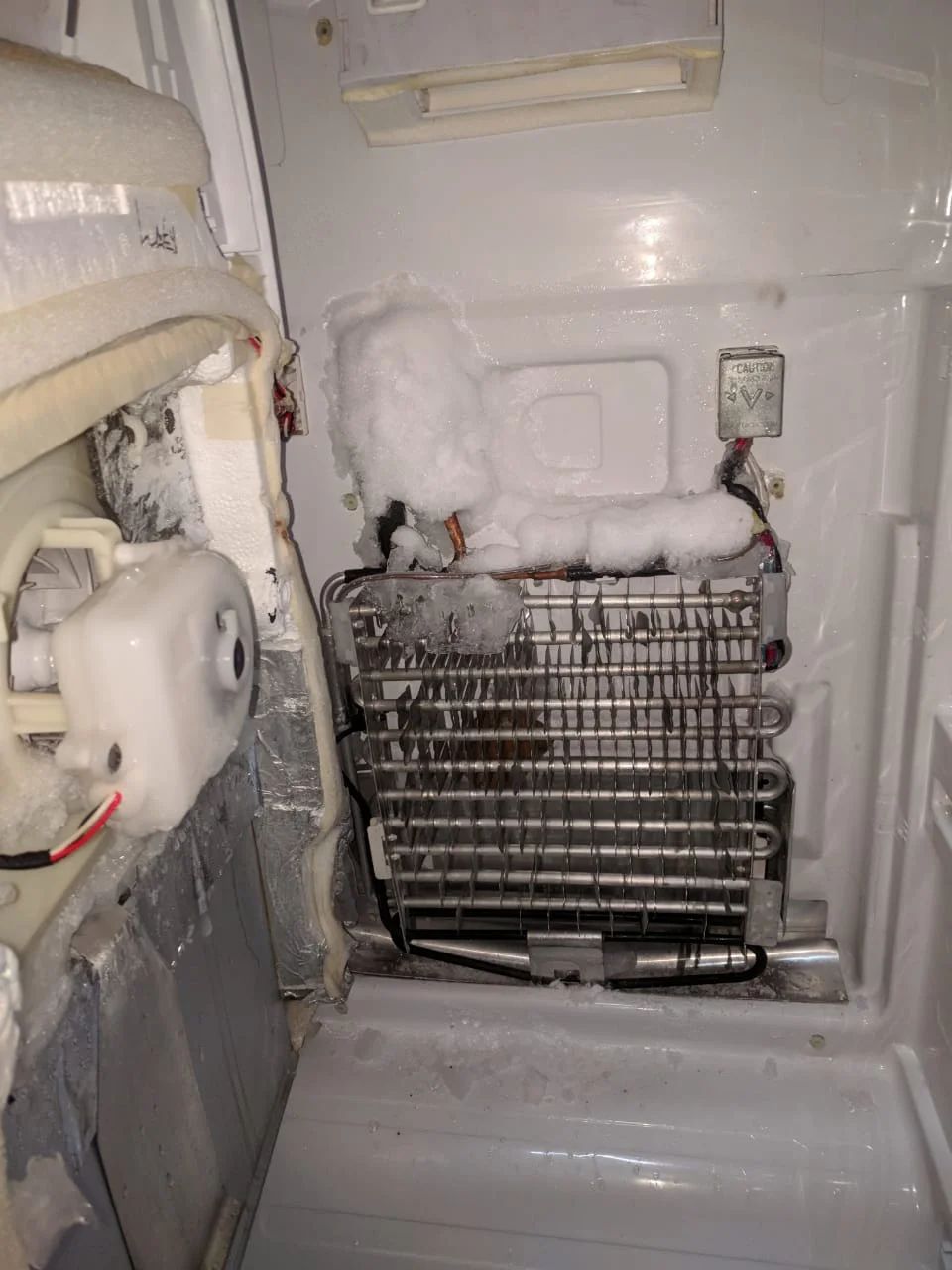 The inside of a refrigerator is covered in snow and ice.
