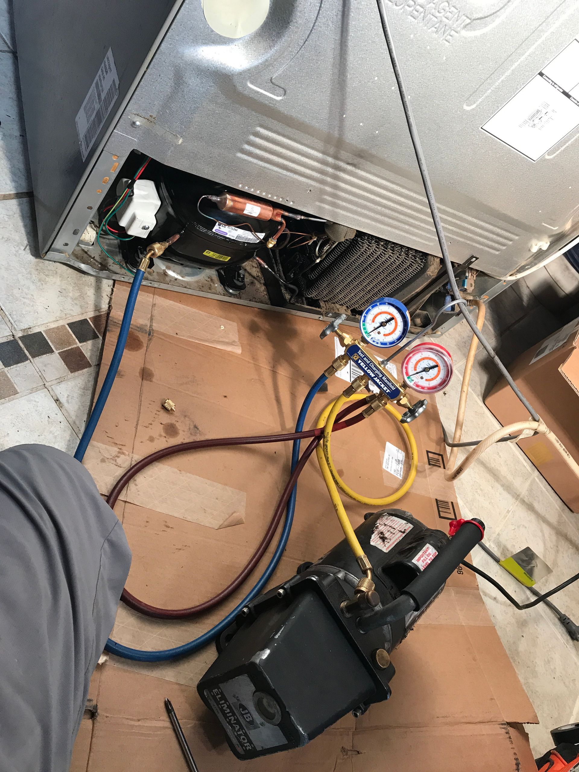 A person is working on a refrigerator with a vacuum pump attached to it.