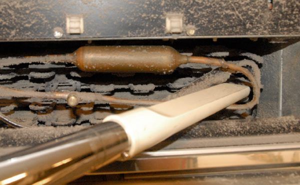 A vacuum cleaner is being used to clean the inside of a refrigerator.