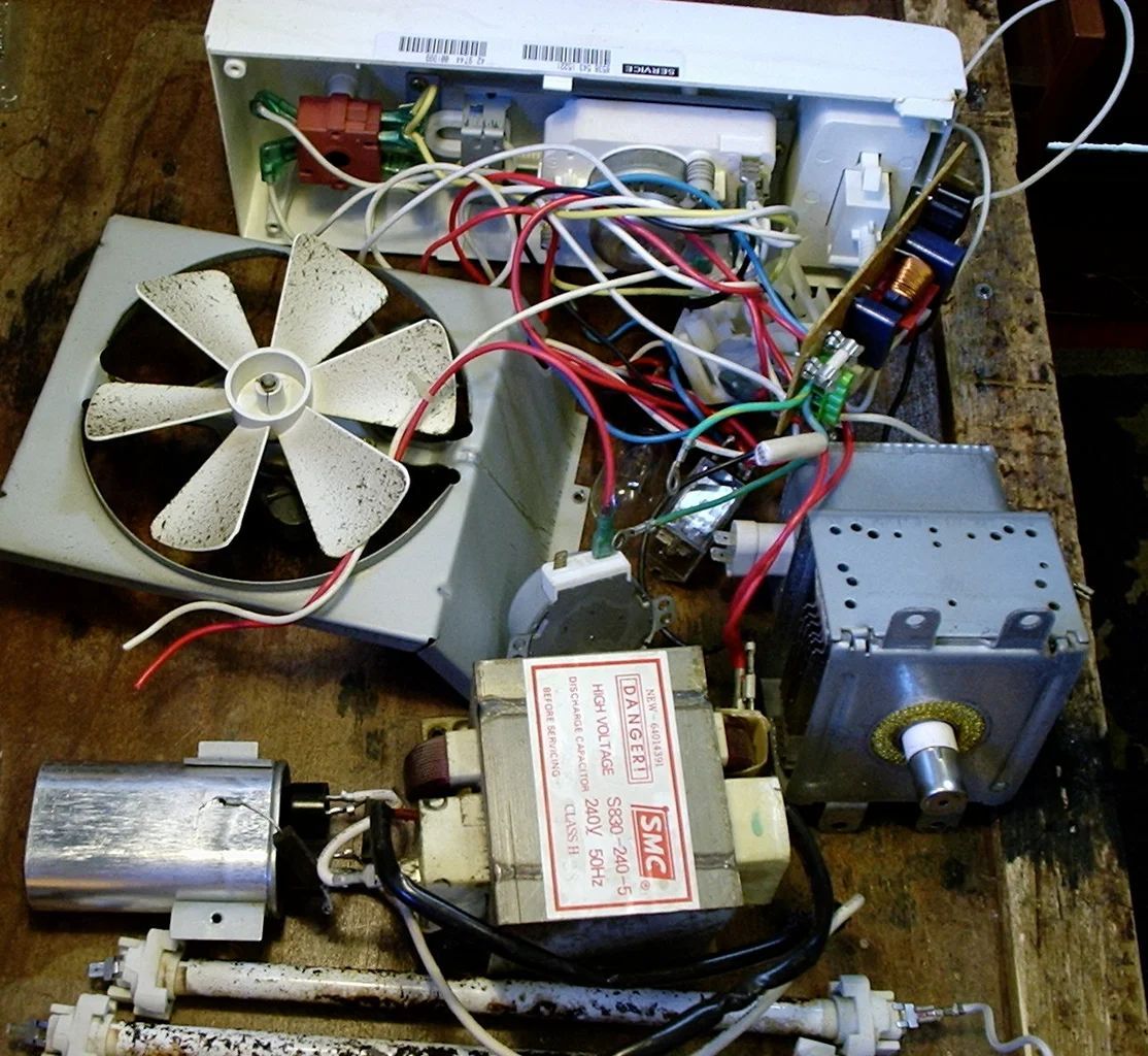 A fan is sitting on a wooden table next to a microwave and a transformer